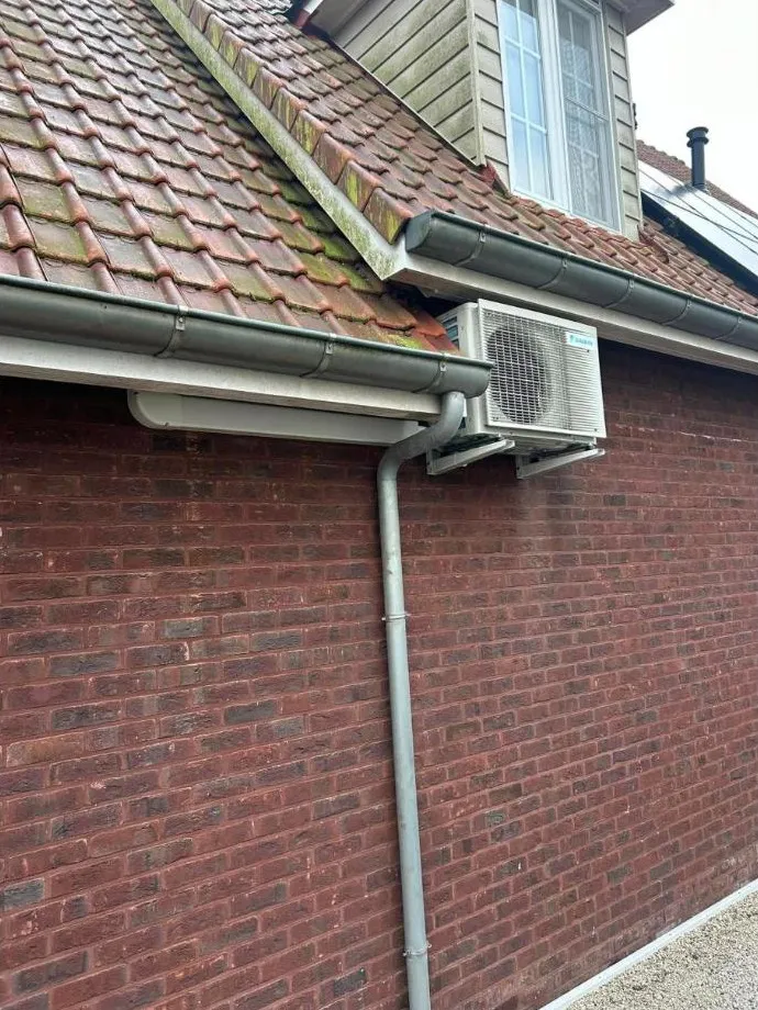 Daikin-buitenunit op consoles onder de dakgoot, tegen een bakstenen gevel